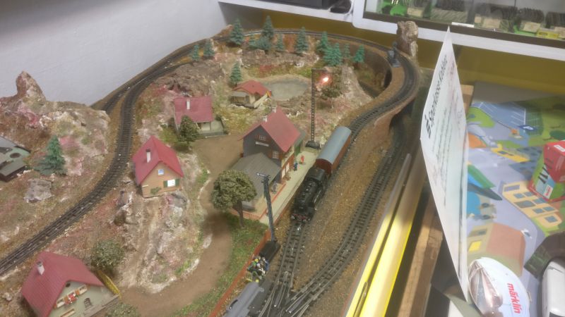 Hier steht die Lok mit ihrem Güterwagen stumm, starr und sprachlos vor dem Bahnhofsgebäude. Auf der kleinen Trix H0 Anlage mit dem verrückten Gleisplan ist sogar Platz für das kleine Stilleben.