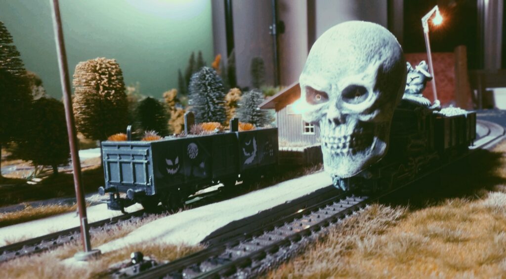 Düster überflutet fahlblaues Mondlicht den Bahnsteig von Heimbuchenthal. Der einsame Friedhofswagen steht verlassen auf dem Gütergleis am Schuppen. Die Leuchte am Bahnsteig kämpft mit der Düsternis, weiß sie doch, dass sie diesen Kampf noch vor Mitternacht verlieren wird. Derweil ahnt der Märklin 44232 Halloween Wagen "Glow in the Dark" auf seinem Abstellgleis Übles, als die Märklin 3029 Tenderlokomotive ihre knöcherne Galionsfigur in den Bahnhof schiebt. Finster blicken die tiefroten Augen des Totenschädels, nichts Gutes verkündend.
